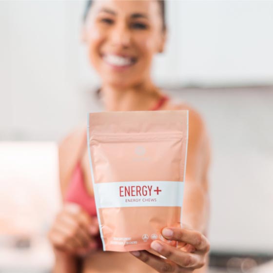 Woman blurred in background holding packet of Neora’s Energy+ Wellness Chews.